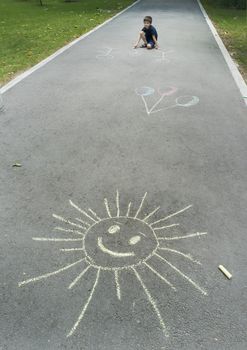 Child drawing sun on asphalt in a park