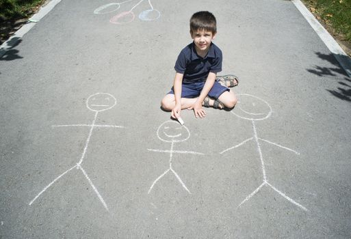 Child drawing family on asphalt in a park
