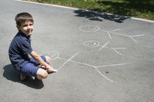 Child drawing family on asphalt in a park