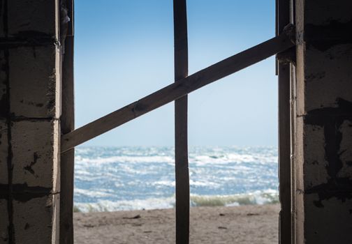 cross of boards in the window overlooking the sea and the beach