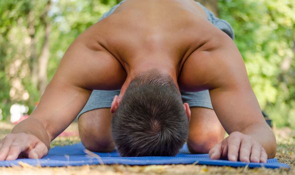 young athletic sunburnt man in balasana yoga pose on a blue mat