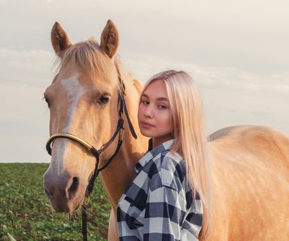portrait of a young blonde girl with a beige horse on the ranch closeup
