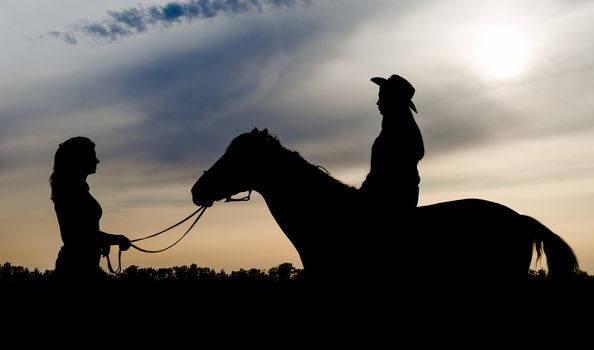 silhouette of two young girls with hat and horse on sunset background