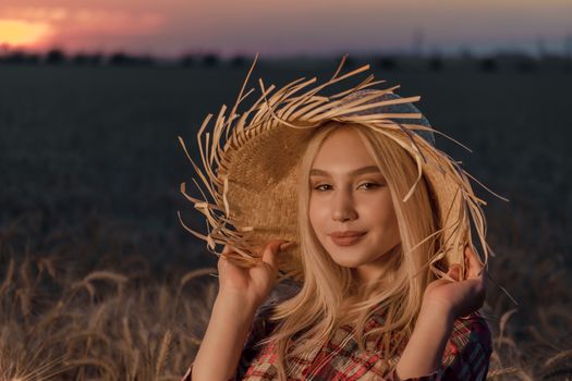 portrait of a young girl in a straw hat on the background of a wheat field and sunset in the evening closeup