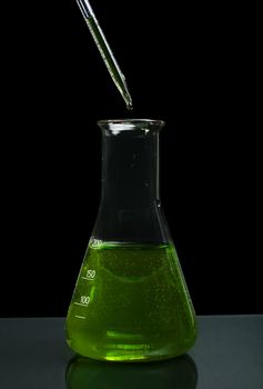 Laboratory beaker filled with green color liquid substances and laboratory pipette. Dark background