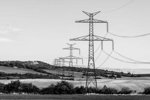 Line of transmission towers, or electricity pylons, in the rural landscape. Black and white image.