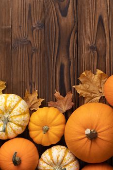 Striped yellow and orange pumpkins and dry maple autumn leaves on wooden background, top view, Halloween concept