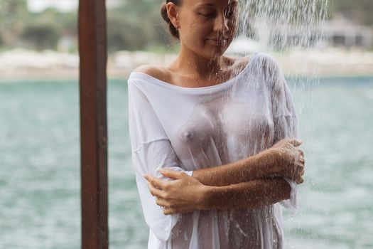 Crop young lady in wet white blouse embracing herself trying to avoid splash of clean water