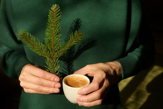 Woman is holding pine tree branch and an espresso cup