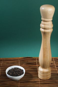 Bowl with black pepper and wooden pepper mill on wooden base