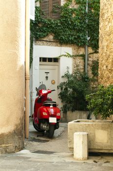 Small red scooter parked at the old quarter buildings. St. Tropez buildigs.