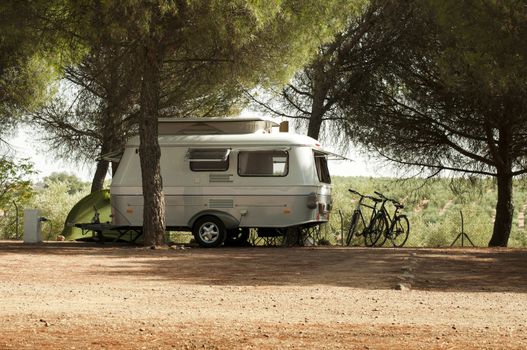 Small white caravan through the trees. Green tent and bikes.