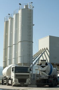 Cement factory and two white trucks loading cement