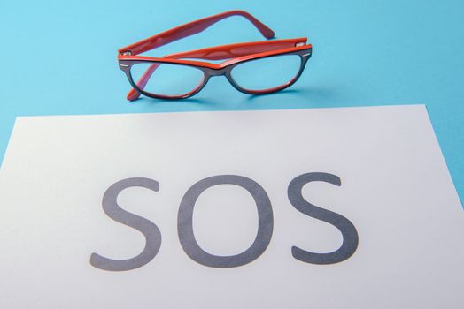 Word SOS written on white paper. Blue background