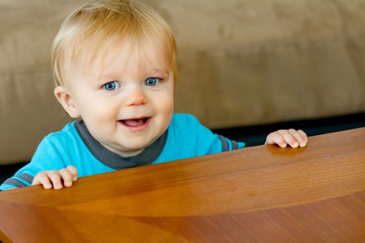 Toddler against the table trying to hold himself up while learning out how to walk and making a huge smile.
