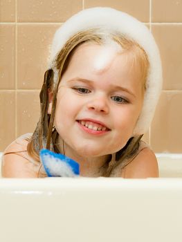 Young girl playing with a random toy in the bathtub while covered in suds