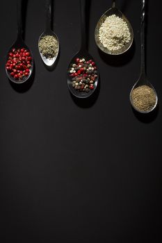 Spices in metal spoons on a black background