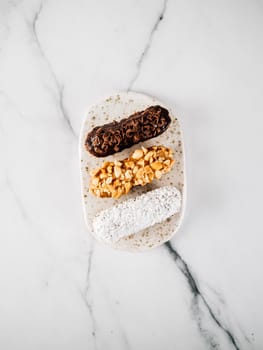 Set of three homemade eclairs on marble background. Top view of delicious healthy profitroles with different decor elements - chocolate, peanut and sherdded coconut. Vertical