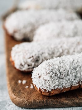 Homemade eclairs with coconut on wooden cutting board. Close up view of delicious healthy profitroles with shredded coconut. Copy space for text or design. Vertical.