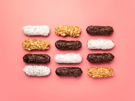 Set of different homemade eclairs on pink background. Top view of delicious healthy profitroles with different decor - chocolate, peanut and sherdded coconut