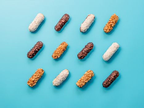 Set of different homemade eclairs on blue background. Top view of delicious healthy profitroles with different decor elements - chocolate, peanut and sherdded coconut