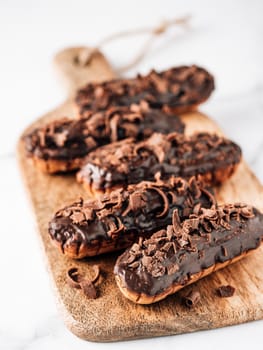 Homemade eclairs with chocolate on wooden cutting board. Close up view of delicious healthy profitroles with chocolate glaze. Copy space for text or design. Vertical.