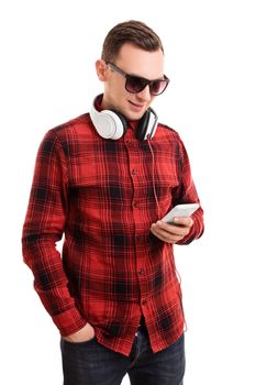 Modern and casual in style. Portrait of a confident smiling man or student in plaid shirt, sunglasses and headphones, looking at his mobile phone and texting, isolated on a white background.