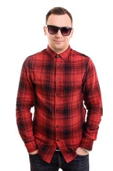 Modern and casual in style. Fashion portrait of stylish handsome young man in plaid shirt and sunglasses, posing with hands in pockets, isolated on white background.