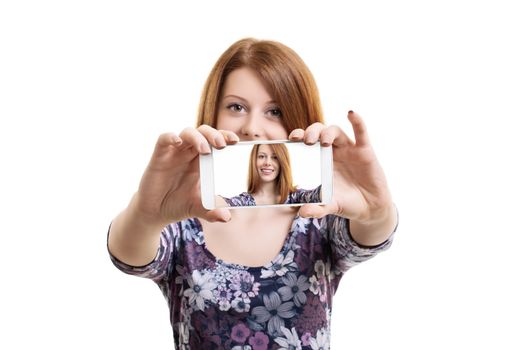 Beautiful smiling fashionable young woman taking a selfie with a smartphone, isolated on a white background.
