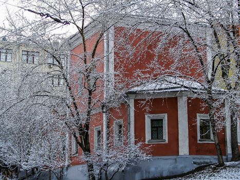 Winter city in the snow. The red building stands surrounded by snow-covered trees.