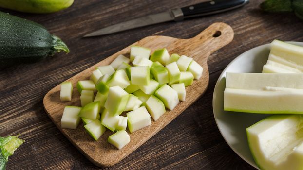 Zucchini harvest. Slices farm organic zucchini cubes for freezing on woodencutting board over brown wooden table. Zucchini harvesting concept.