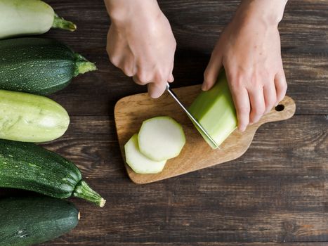 Zucchini harvest. Woman slices zucchini on wooden table. Farm organic zucchini harvesting