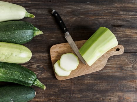 Sliced fresh organic zucchini on wooden cuttingboard over brown wooden table. Zucchini harvesting concept. Top view or flat lay.