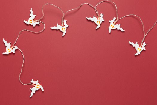 Christmas wooden garland with warm light in form of white running deers on dark red background. Blank for postcard layout. Festive, New Year concept. Horizontal, flat lay. Minimal simple style.