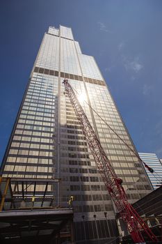 Chicago skyscraper against blue sky, with construction crane at it’s base