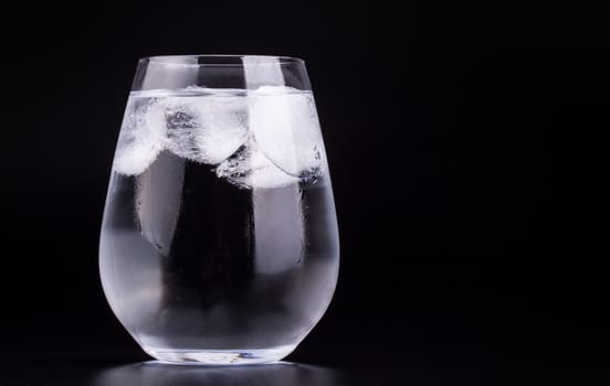 Big glass of water with ice cubes, black background