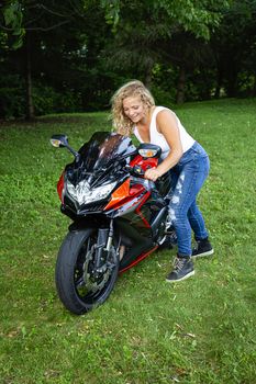 Young blond woman pushing her motocycle in the grass