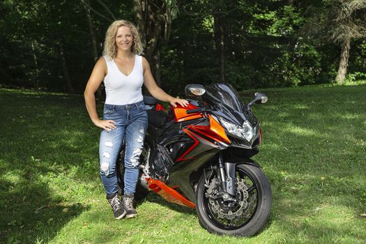 twenty something blond woman, standing beside her sport motocycle, in a park