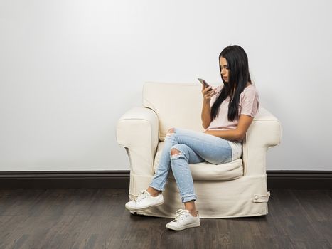 young woman sitting on a white couch, looking at her phone