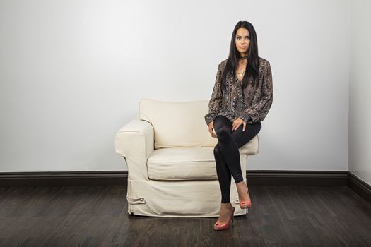 Young woman, in stylish clothes, sitting on the arm of a white couch