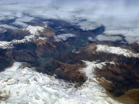 Top view of the ground from the plane. Mountain peaks of the Alps, covered with snow, among the clouds. Soft focus.