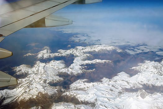Top view of the ground from the plane. Mountain peaks of the Alps, covered with snow, among the clouds. Soft focus.
