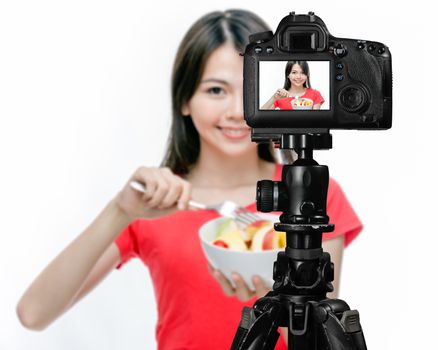 Asian food vlogger with fruit salad behind camera, social media production concept