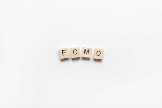 Abbreviation word FOMO from wooden blocks on white background. FOMO means Fear Of Missing Out, non-stop internet surfing. Concept social communication problem between people, digital detox. Flat lay.