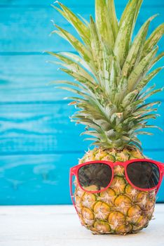 Holiday pineapple have sunglasses on blue wooden background, tropical holiday concept