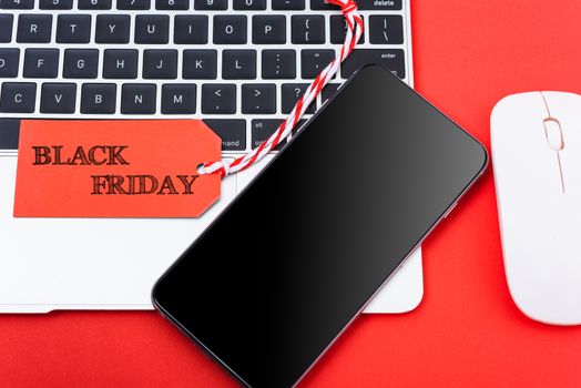 Black Friday Sale text on red tag have mobile smart phone over laptop computer with red background