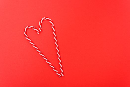 Two candy canes made making Heart of Christmas candies on red background with copy space