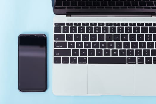 Top view of modern technology smart phone mobile and computer laptop on blue background with copy space