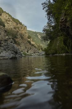 Rock face covered with vegetation is the boundary of the watercourse in the mountains with various rocks that rise from the water: The view of Sa Stiddiosa in the heart of Sardinia.