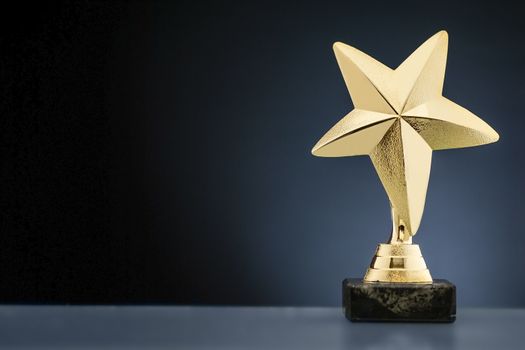 Championship or race trophy with a gold star on a plinth placed to the side over blue with copy space to be awarded to the winner of a competition
